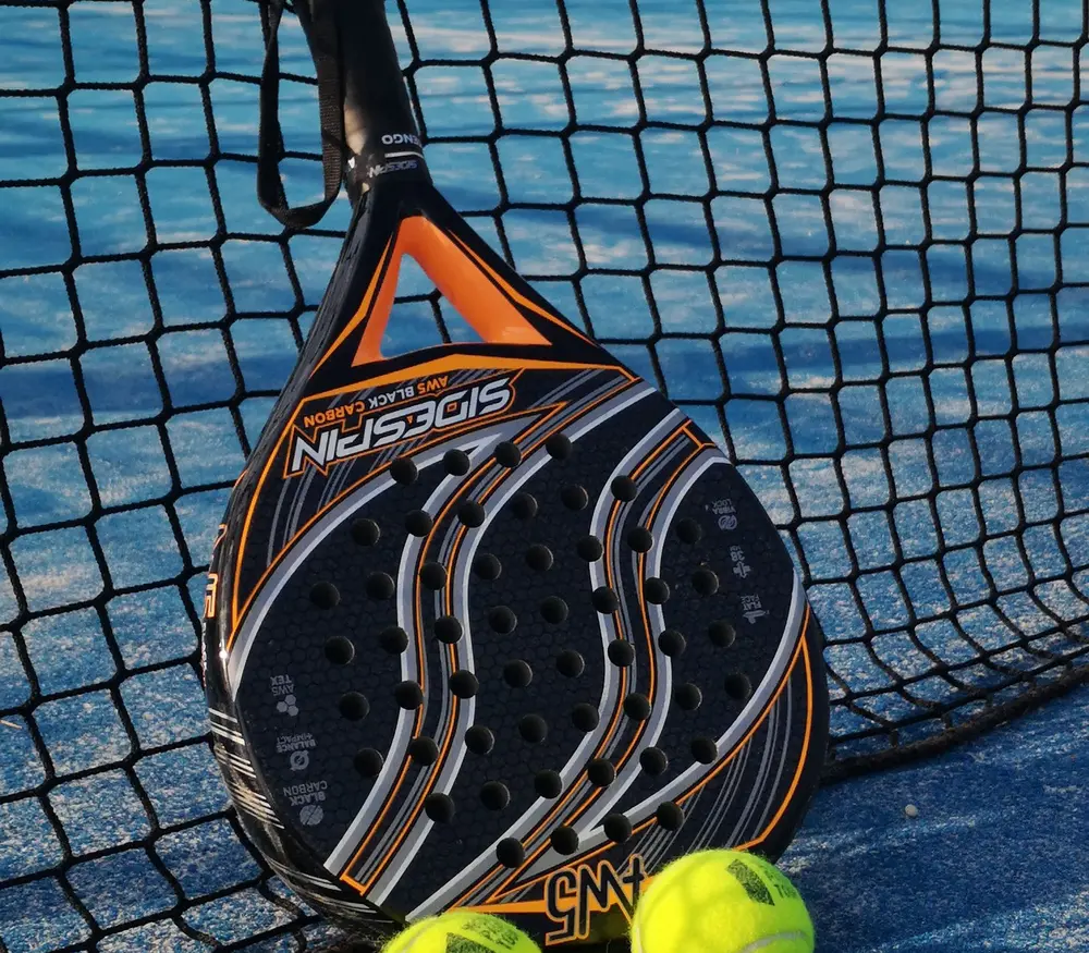 Raquette de padel et balles jaunes contre le grillage d'une piste