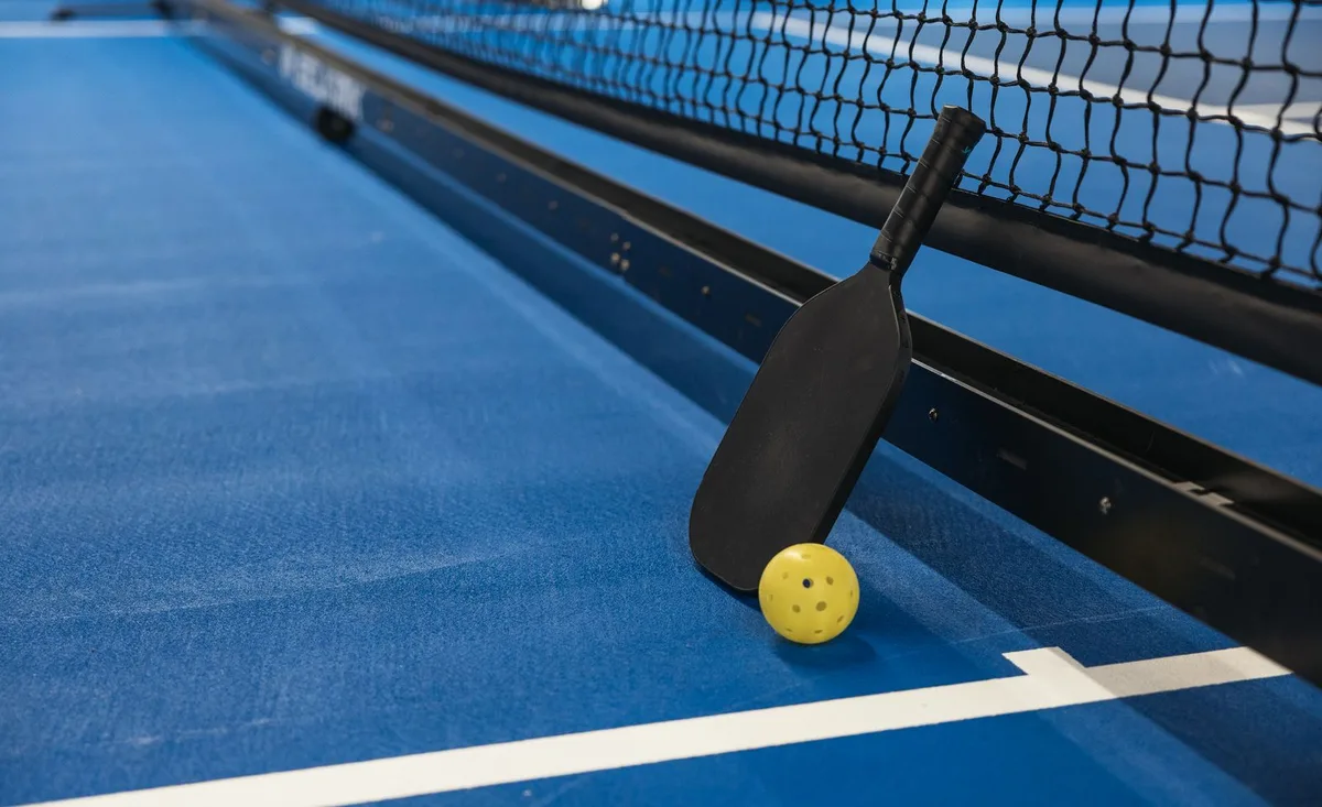 Paddle de pickleball et balle perforée posés sur un terrain bleu